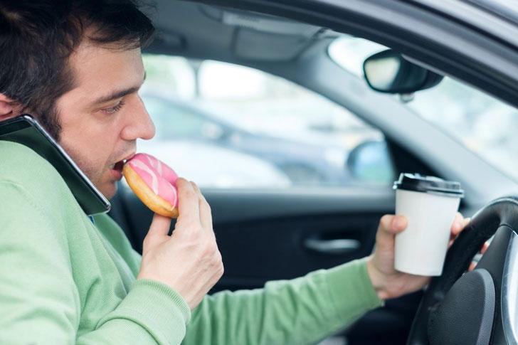 man eating doughnut while driving his car